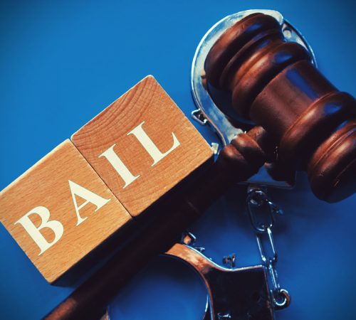 word bail composed of wooden dices. wooden gavel and statue of themis in the background.